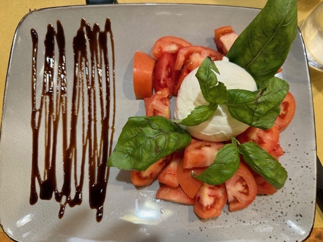 A plate featuring sliced tomatoes arranged around a ball of fresh mozzarella, garnished with basil leaves and drizzled with balsamic reduction.