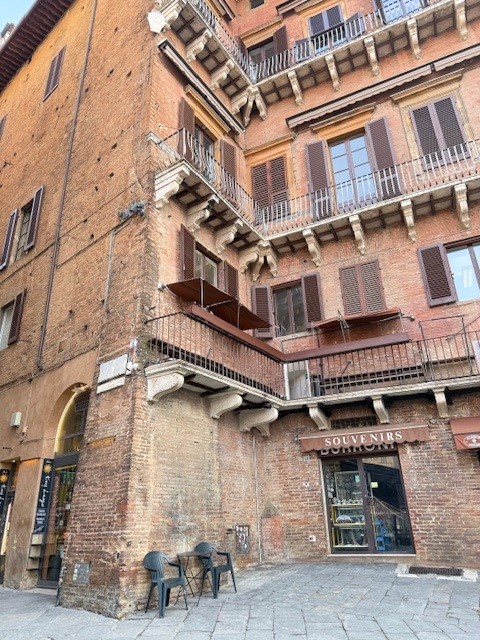 Corner of a brick building featuring multiple balconies, with a shop labeled 'Souvenirs' at the base and outdoor seating.
