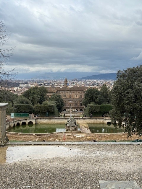 View of a historic garden with a fountain in the foreground, overlooking the cityscape of Florence under a cloudy sky.