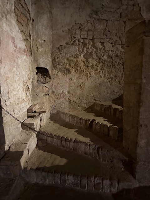 Dimly lit staircase in an old stone structure, featuring worn steps and rough walls.
