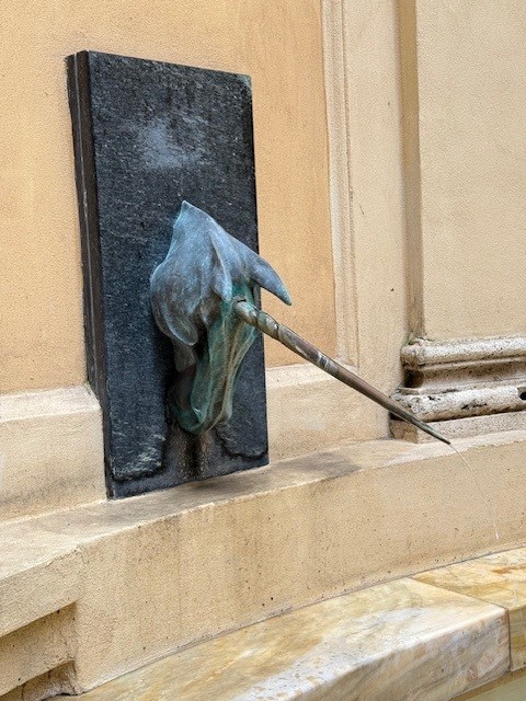 A bronze sculpture of a unicorn's head protruding from a stone wall, featuring a detailed mane and a long horn.